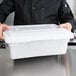 A person wearing a black coat holding a white Choice plastic food storage container.