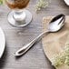 A Reed & Barton Holliston stainless steel dessert spoon on a napkin next to a glass of ice cream.