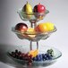 A Clipper Mill stainless steel wire stand holding a three tiered glass bowl with fruit.