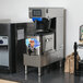 A Curtis G4TBP Polaris tea brewer on a counter in a corporate office cafeteria with a black drink dispenser and screen.