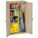 A Tennsco putty metal janitorial cabinet with shelves holding cleaning supplies and mops.