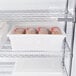 A white plastic food storage container on a white surface with a close up of a plastic bag of food inside.