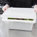 A person holding a Choice white plastic food storage box lid over a container of food.