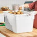 A large white polyethylene food storage box filled with potatoes on a wooden countertop.