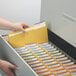 A hand putting a yellow Smead file folder in a file cabinet.