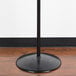 A Marco Company black metal floor mount produce bag stand with a black pole.