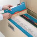 A person using a blue Smead legal size file folder to open a file cabinet.