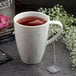 A Schonwald white porcelain mug filled with tea and a tea bag with flowers on the table.