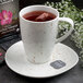 A Schonwald white porcelain mug filled with tea and a tea bag on a saucer.