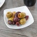 A Schonwald square porcelain bowl filled with green olives on a table.