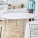 A man standing near a Lancaster Table & Seating white folding table.