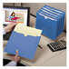 A hand holding a blue Smead file jacket in front of a computer screen.