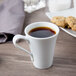 A Schonwald white porcelain espresso cup filled with coffee on a saucer with cookies and a spoon.