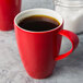 A close-up of a red Schonwald porcelain mug with a brown liquid in it.