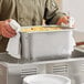 A man holding a Vollrath stainless steel steam table pan with food in it.