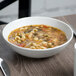 A white Schonwald round porcelain bowl filled with soup, pasta, and vegetables.