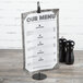A Clipper Mill black powder coated iron wire table card holder with a menu next to salt and pepper shakers.