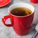 A Schonwald red porcelain cup filled with tea on a table.