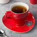 A red Schonwald porcelain cup with a tea bag on a saucer.