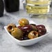 A white Acopa square sauce cup filled with green olives.
