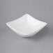 An Acopa bright white square porcelain sauce cup on a gray surface.