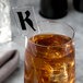 A glass of liquid with ice and a WNA Comet clear rectangular stirrer.
