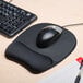 A Fellowes black mouse pad with a foam wrist rest with a mouse on it next to a keyboard.