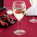 A Libbey tall wine glass filled with white wine on a table next to grapes.