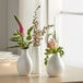 A small, bright white porcelain bud vase holding a floral arrangement.