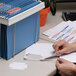 A hand using a Smead white hanging folder tab to label a piece of paper.