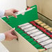 A hand opening a green Smead file jacket in a file cabinet.