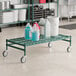 A green metal Regency dunnage cart with bottles and white buckets on it.