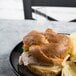 A sandwich with meat and cheese on a clear rectangular plastic pick on a black plate.