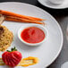 A plate of food with rice, carrots, and a white sauce cup on the side.