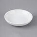 A Choice bright white porcelain round sauce cup on a gray surface.