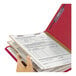 A hand holding a red Smead SafeSHIELD legal size classification folder with documents inside.