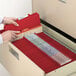 A hand opening a file cabinet drawer with a red Smead SafeSHIELD Legal Size Classification Folder inside.