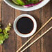 An Acopa bright white porcelain round sauce cup filled with soy sauce on a table with a bowl of food and chopsticks.