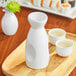 A white Acopa sake bottle and cups on a wooden tray.