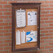 A wooden framed Aarco bulletin board with cork and papers attached.