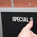 A person pointing to a black felt message board with white letters.