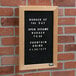 An Aarco black felt open face message board with white text that says "Burger of the Day" on a table in a farm-to-table restaurant.