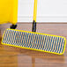 A yellow Rubbermaid HYGEN microfiber mop pad with blue corners on a wood floor.