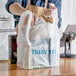 A person in a brown apron holding a white plastic "Thank You" T-shirt bag.