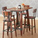 A Lancaster Table & Seating solid wood live edge table top with an antique walnut finish on a table with chairs and glasses.