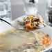 A Libbey stainless steel bouillon spoon filled with soup over a bowl of soup.