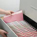 A person opening a file cabinet with a pink Smead file folder.