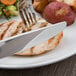 A Libbey stainless steel serrated dinner knife on a plate of food with a fork