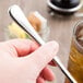 A person holding a Libbey stainless steel iced tea spoon over a glass of iced tea.