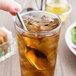 A hand using a Libbey stainless steel iced tea spoon in a glass of iced tea.